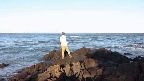 A-fisherman-stands-on-coastal-rocks-in-Southern-Australia-and-casts-a-rod-into-the-water