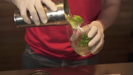 Barman-pours-mojito-from-mixer-into-glass,-slow-motion