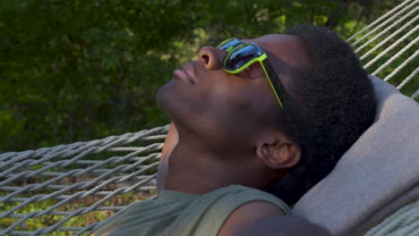 Black-Man-with-sunglasses-lying-on-swinging-hammock-outdoors,-close-up