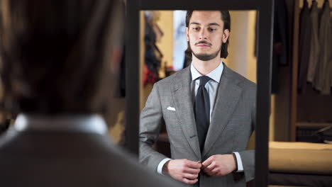Mirror-reflection-of-young-man-buttoning-suit-in-fashion-boutique