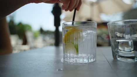 Hand-uses-a-straw-to-mix-a-glass-of-water-with-ice-cubes,-lemon-and-lime-in-it