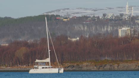 small-white-boat-sailing-along-the-fjord-in-northern-norway,-telephoto-shot-in-60fps-slow-motion