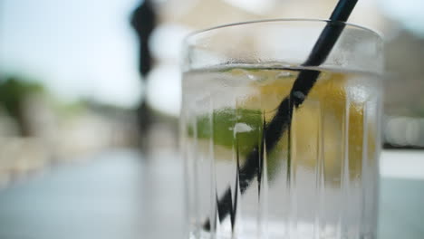 Hand-lets-go-of-a-straw-after-mixing-glass-with-water,-lemon-wedge,-lime,-and-ice-cubes