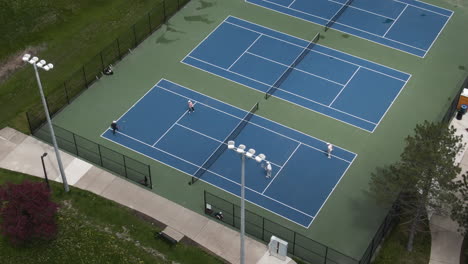An-aerial-close-up-shot-of-hard-tennis-courts,-where-players-are-playing-doubles