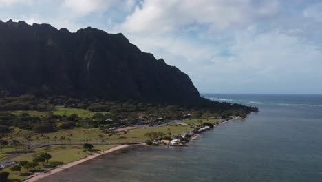 Cinematic-drone-shot-of-a-jagged-mountainside-contrasted-by-clear-blue-water-on-the-coast-of-Oahu's-North-Shore