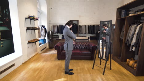 Young-man-trying-on-suit-in-front-of-classy-boutique-mirror,-zoom-shot