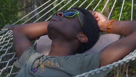 Young-Black-Man-resting-on-swinging-hammock-outdoors-hands-behind-his-head