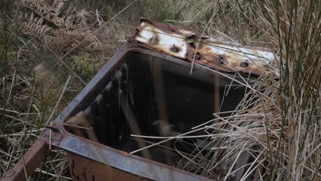 Handheld-shot-of-illegal-waste-dumped-in-the-nature,-rusty-metal-in-a-field