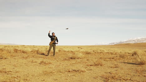 Slow-motion-shot-of-a-Predator-falcon-bird-flying-in-to-catch-food-from-the-hand-of-a-man-on-a-barren-land-at-daytime