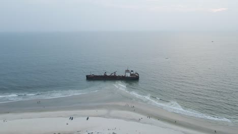 Aerial-view-of-tourist-visiting-old-rusty-wreck-at-sandy-beach-with-sea-in-background