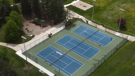 An-aerial-shot-of-hard-tennis-courts,-where-players-are-playing-doubles