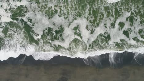 Aerial-shot-panning-right-over-dark-beach-with-green-water-and-waves-in-Northern-California