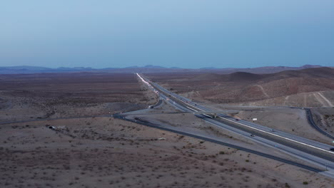 Descending-aerial-view-of-cars-driving-on-highway-through-desert-at-dusk,-California