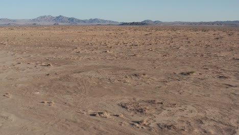 Flying-low-over-bleak-and-empty-desert-landscape-with-distant-mountains