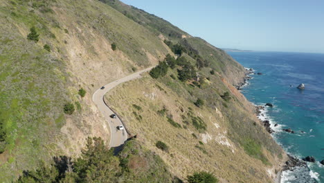 Cars-drive-scenic-coastal-Highway-1-in-California-overlooking-ocean-on-sunny-day