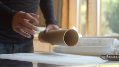 An-architect-or-designer-pulls-rolls-of-construction-plans-out-of-a-cardboard-tube
