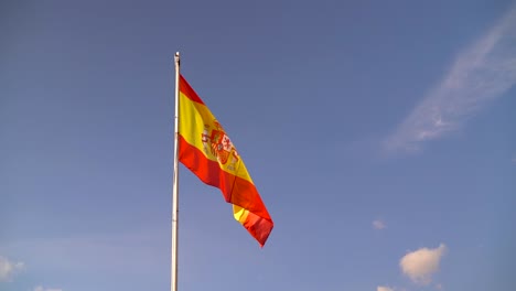 Lebendige-Und-Farbenfrohe-Spanische-Flagge,-Die-In-Zeitlupe-Vor-Blauem-Himmel-Mit-Wenigen-Wolken-Weht