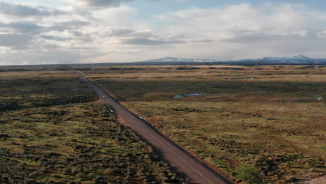 Panoramic-aerial-of-vehicle-driving-through-vast-Idaho-plain-with-mountains