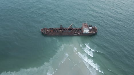 Aerial-top-down-shot-of-old-industrial-ship-wreck-parking-on-shore-of-beach