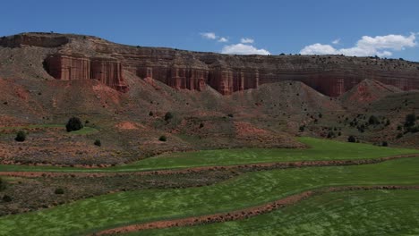 Aerial-drone-view-of-green-grain-fields-waved-by-the-wind-in-a-dessert-red-canyon-in-Teruel,-Spain
