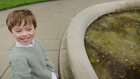 A-young-boy-is-sitting-in-the-garden-enjoying-the-fountain-water-and-having-fun-with-it