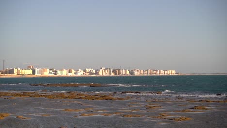Low-tide-ocean-view-towards-city-skyline-with-slow-motion-waves
