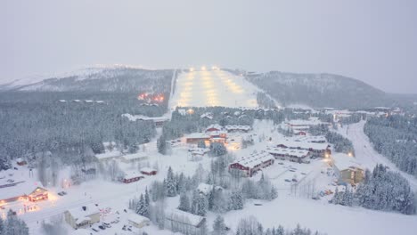 Drone-aerial-push-in-Levi,-Finland-ski-resort,-snowy-ski-town-with-pine-trees-and-ski-slopes