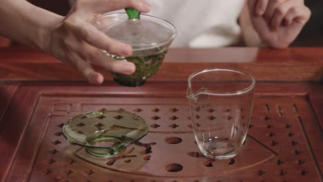 Pouring-infused-green-tea-from-gaiwan-into-the-glass-on-traditional-dark-wood-tea-table