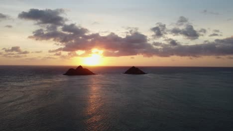 Cinematic-zoom-out-drone-shot-of-the-sunrise-behind-two-islands-off-the-Lanikai-coast-on-the-Island-of-Oahu-in-Hawaii