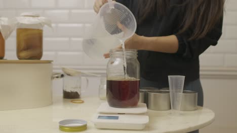 Woman-adds-water-inside-the-barrel-with-infused-tea-on-top-of-digital-scales