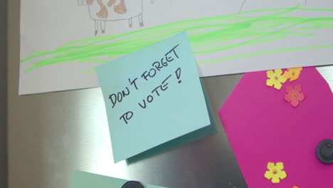 A-person's-hand-sticks-a-reminder-on-the-refrigerator-door-with-the-handwritten-message,-Don't-forget-to-vote