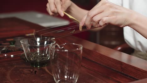 Gießen-Sie-Chinesische-Grüne-Teeblätter-In-Ein-Teeglas-Aus-Glas