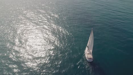 Drone-flying-away-from-sailboat-and-tilting-into-the-horizon-near-the-coastline