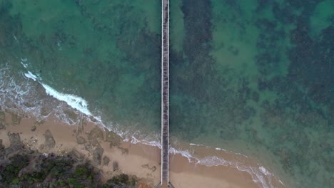 Vertical-slow-moving-drone-view-along-the-Point-Lonsdale-pier,-Victoria,-Australia