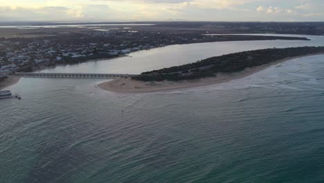 Reverse-aerial-footage-looking-upstream-near-the-mouth-of-the-Barwon-River-at-Barwon-Heads-with-Lake-Connewarre-in-the-background,-Victoria,-Australia