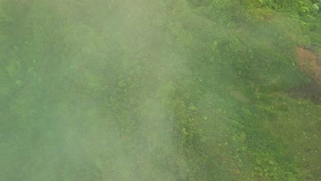 Overhead-view-of-fog-passing-over-mountain-covered-by-green-foliage