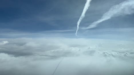 Sky-view-from-a-jet-cockpit-during-flight-overflying-clouds-and-bellow-another-jet-wake