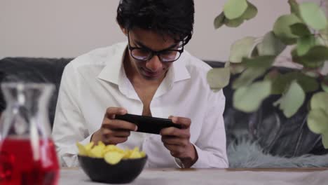 Young-man-playing-games-on-his-phone-while-snacking-on-crisps