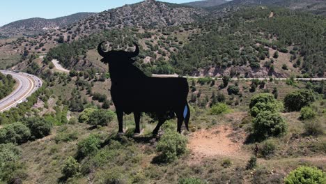Aerial-fordward-drone-view-of-the-spanish-iconic-Toro-de-Osborne,-a-national-symbol,-on-the-top-of-a-hill,-daylight