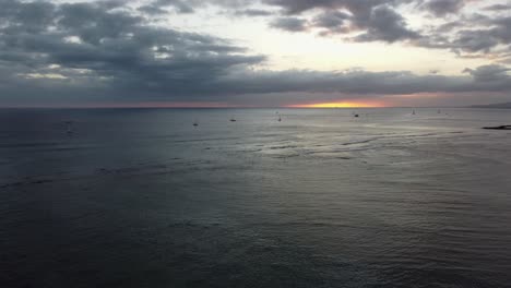 4k-Filmische-Drohnenaufnahme-Des-Sonnenuntergangs-über-Dem-Ozean,-Während-Segelboote-Sitzen-Und-Die-Aussicht-In-Der-Nähe-Des-Waikiki-Strandes-Auf-Oahu-Genießen