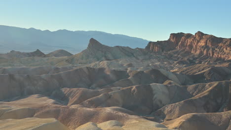 The-hilly-landscape-of-Zabriskie-Point-in-Death-Valley-is-illuminated-by-the-setting-sun,-zoom-out-shot