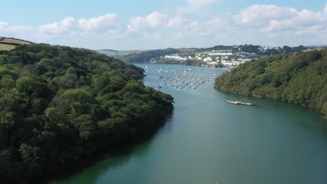 Dramatic-wide-rising-aerial-reveal-from-paddle-boarders-on-the-river-Fowey,-to-reveal-the-Cornish-towns-of-Fowey-and-Polruan-on-the-coast-of-Cornwall,-UK