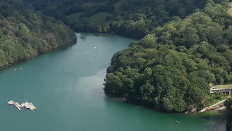 Aerial-view-tilting-up-from-boats-on-the-river-Fowey,-to-reveal-the-surrounding-Cornish-landscape