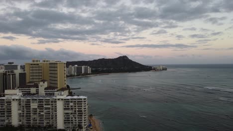 4k-Filmische-Zoom-Out-Drohnenaufnahme-Von-Waikiki-Beach-Und-Diamond-Head,-Während-Die-Sonne-In-Oahu-Untergeht