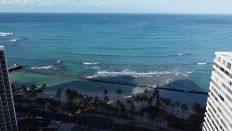 4k-Filmische-Drohnenaufnahme,-Die-Zwischen-Zwei-Waikiki-Hotels-Fliegt-Und-Die-Wellen-Am-Waikiki-Strand-In-Oahu-Beobachtet