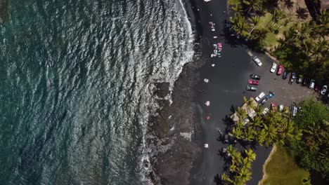 4K-cinematic-overhead-drone-shot-of-ocean-waves-on-Punulu'u-Black-Sand-Beach-with-the-palm-trees-swaying