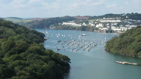 Wide-rising-aerial-reveal-over-the-river-Fowey,-to-reveal-the-dramatic-Cornish-coastline-and-the-towns-of-Fowey-and-Polruan,-UK