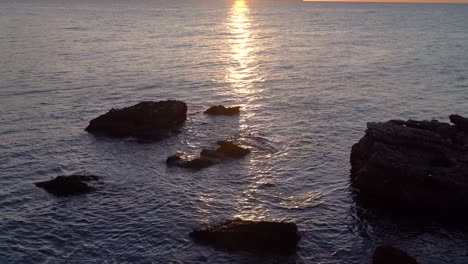 Slow-cinematic-tilt-up-over-rocks-in-ocean-during-sunrise