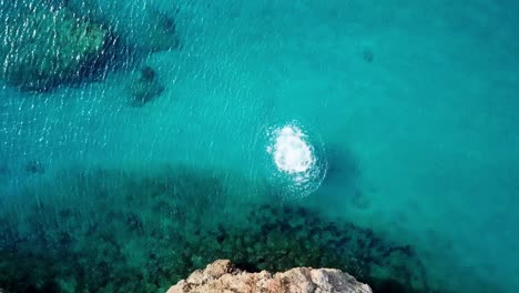 Overhead-view-of-a-young-blond-man-jumping-off-a-cliff-into-the-pristine-waters-of-the-beaches-of-Curacao,-a-Dutch-Caribbean-island