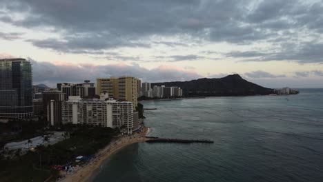 4K-cinematic-crane-drone-shot-of-Waikiki-Beach-and-Diamond-Head-illuminated-by-the-orange-tint-from-the-sunset-in-Oahu